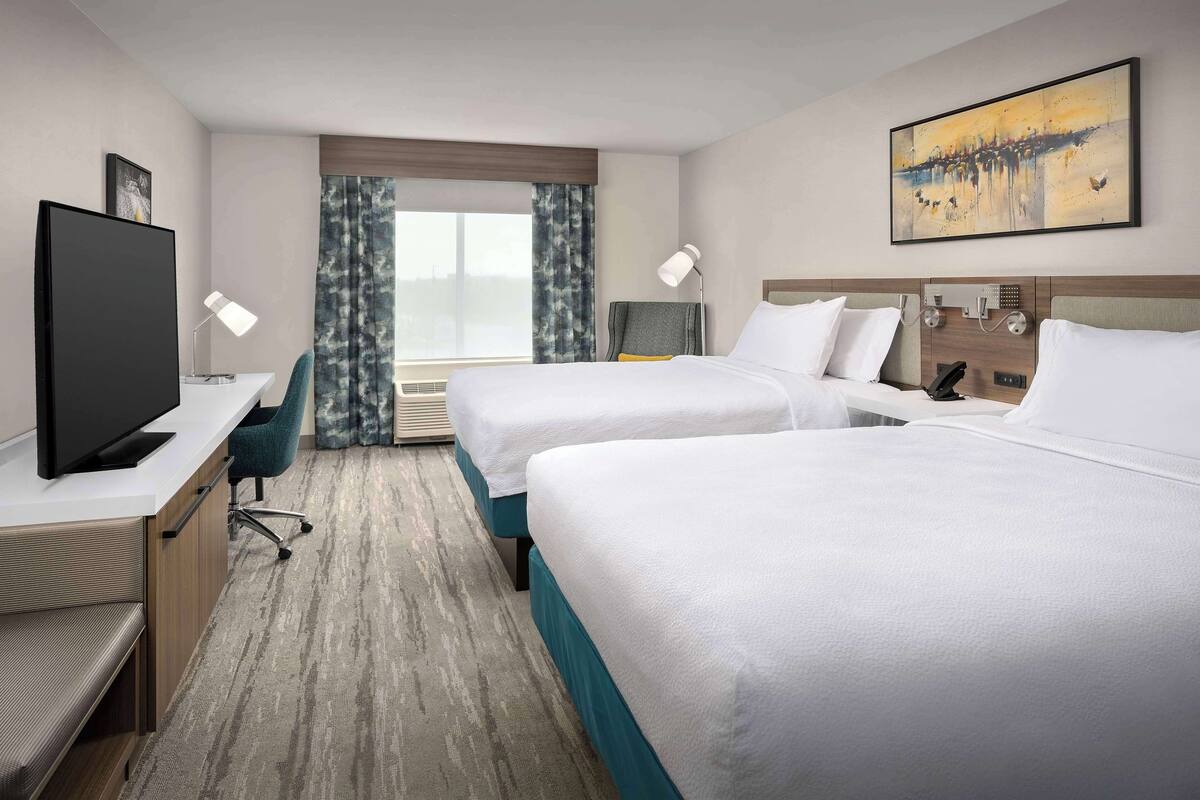 Hotellihuone, jossa on kaksi sänkyä, työpöytä, jossa on televisio, tuoli ja taulu seinällä.