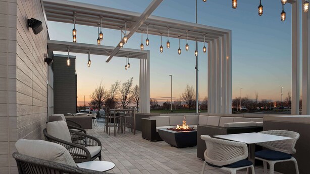 Un patio al aire libre con mobiliario de mimbre, un pozo de fuego y luces colgantes.