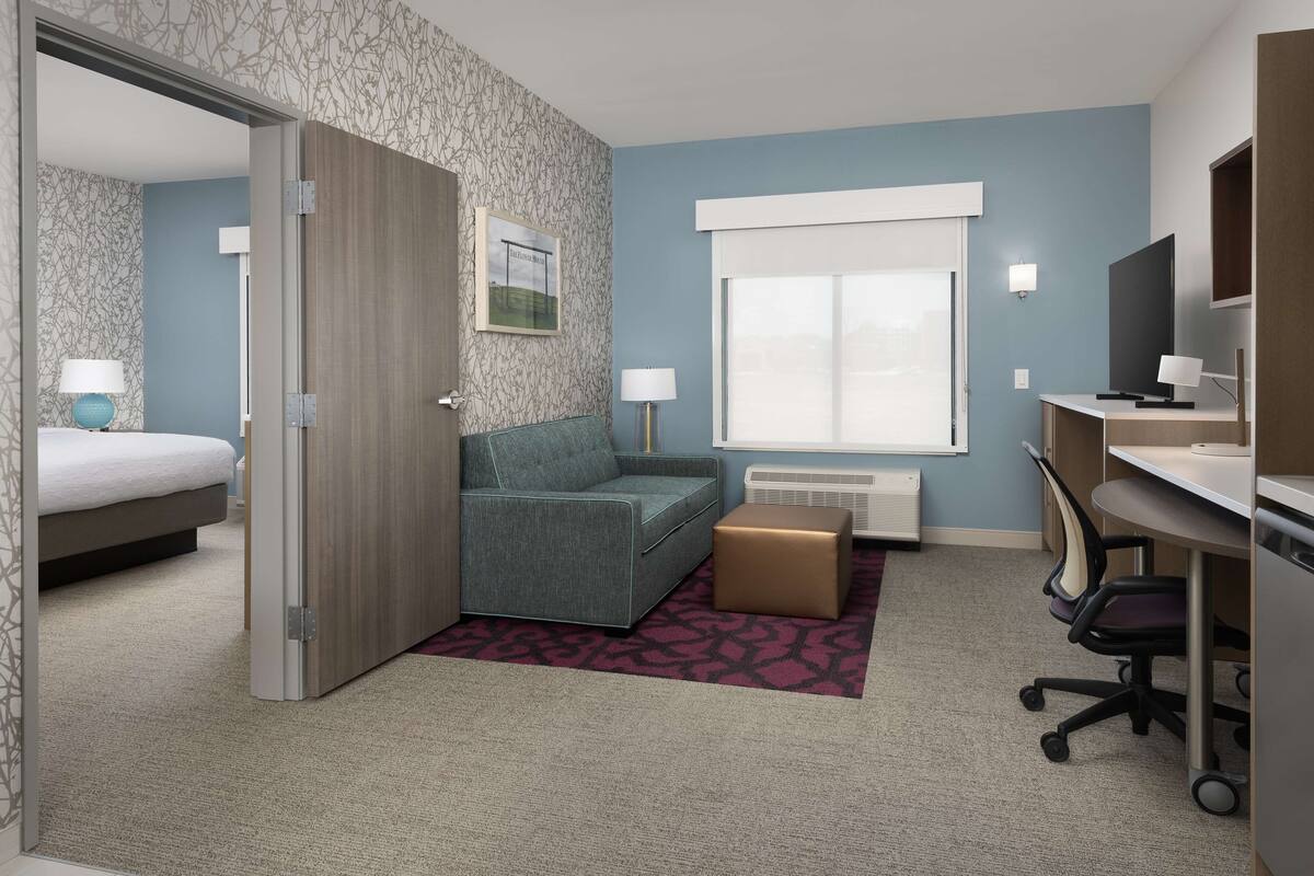 A hotel room with a bed, a sofa, a desk, a chair, a window, and a radiator.