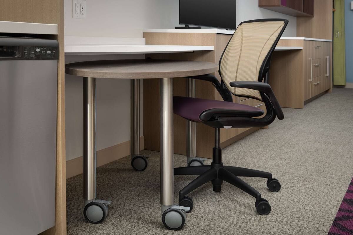 A modern office space with a round table, a cushioned office chair, and a built-in dishwasher.