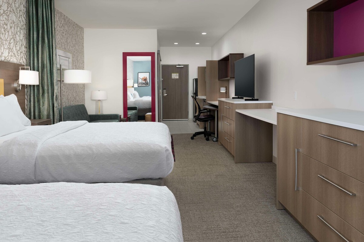 A hotel room with two beds, a desk, a TV, and a wardrobe.