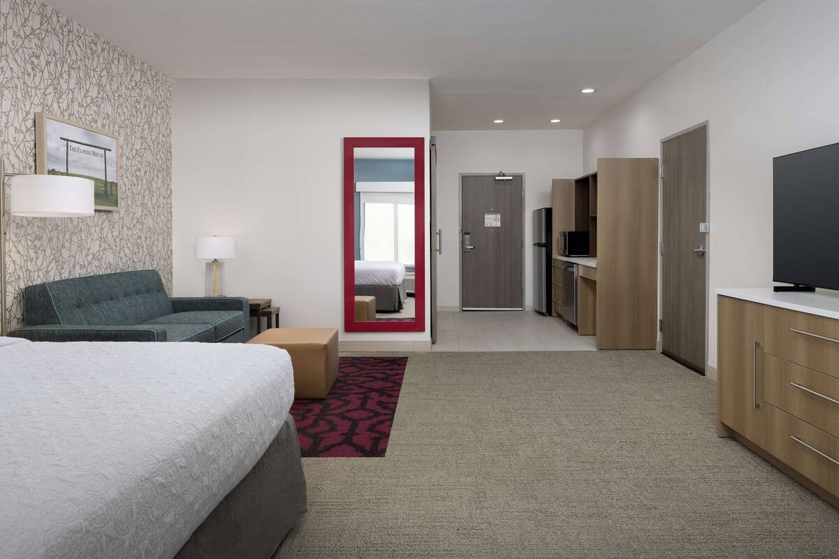 A hotel room with a bed, a sofa, a desk, a TV, and a mirror.