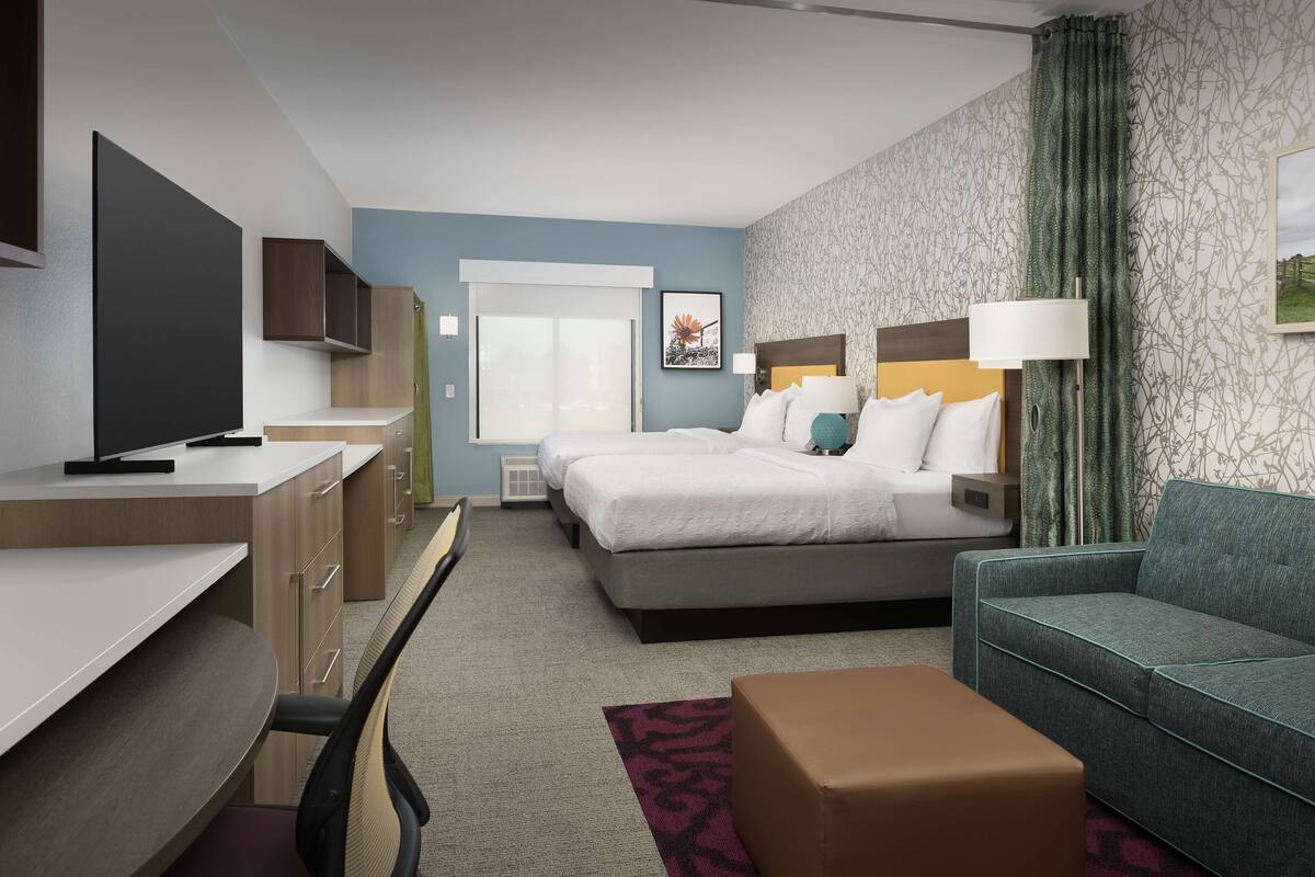 A modern hotel room with a bed, a sofa, a desk, and a television.