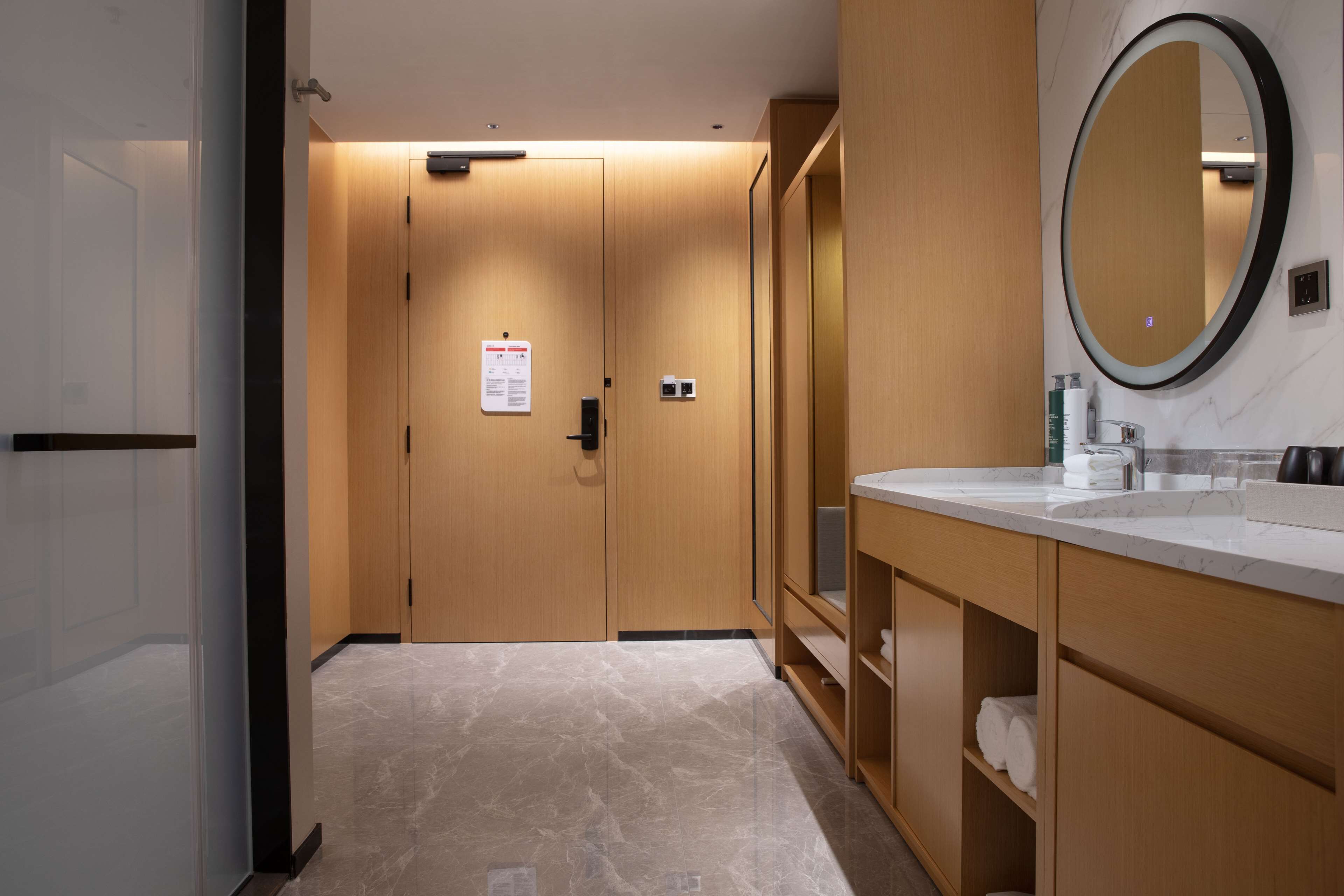 Un baño de hotel con armarios de madera, suelo de mármol, un espejo grande y un lavamanos blanco.