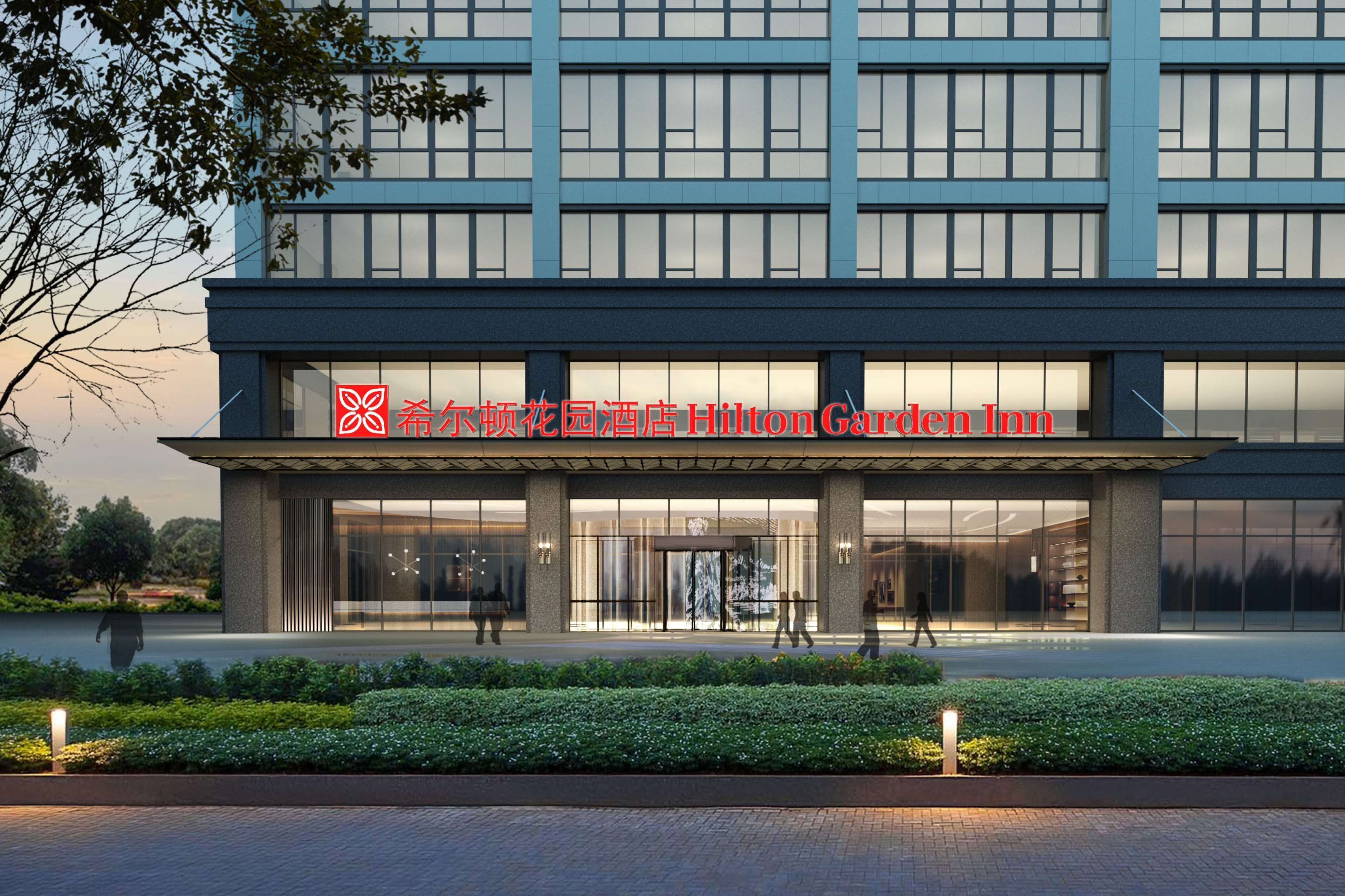 A modern hotel building with a large glass facade, a prominent entrance, and a well-maintained garden area in front.