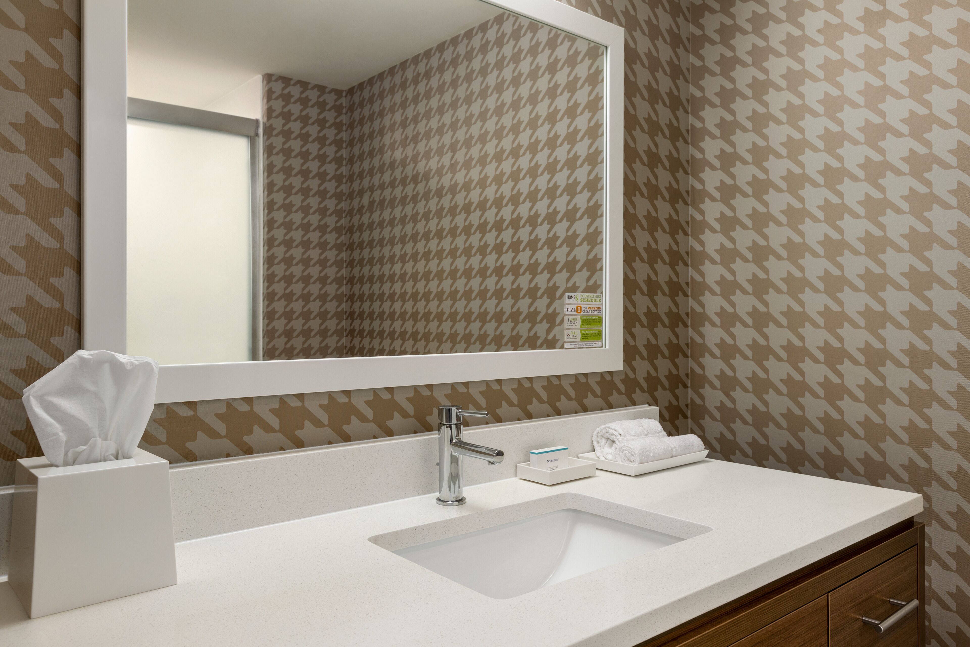 Un baño con lavamanos blanco, un espejo y un perchero para toallas.