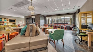 A modern lounge area with a sofa, tables, chairs, and a large window offering a view of the city.
