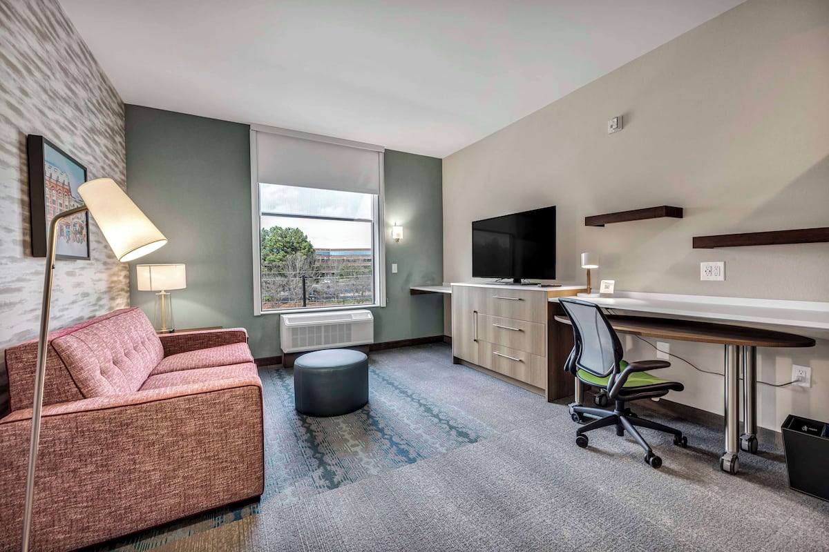 Een moderne hotelkamer met een bank, een bureau, een stoel, een televisie en een raam met uitzicht.