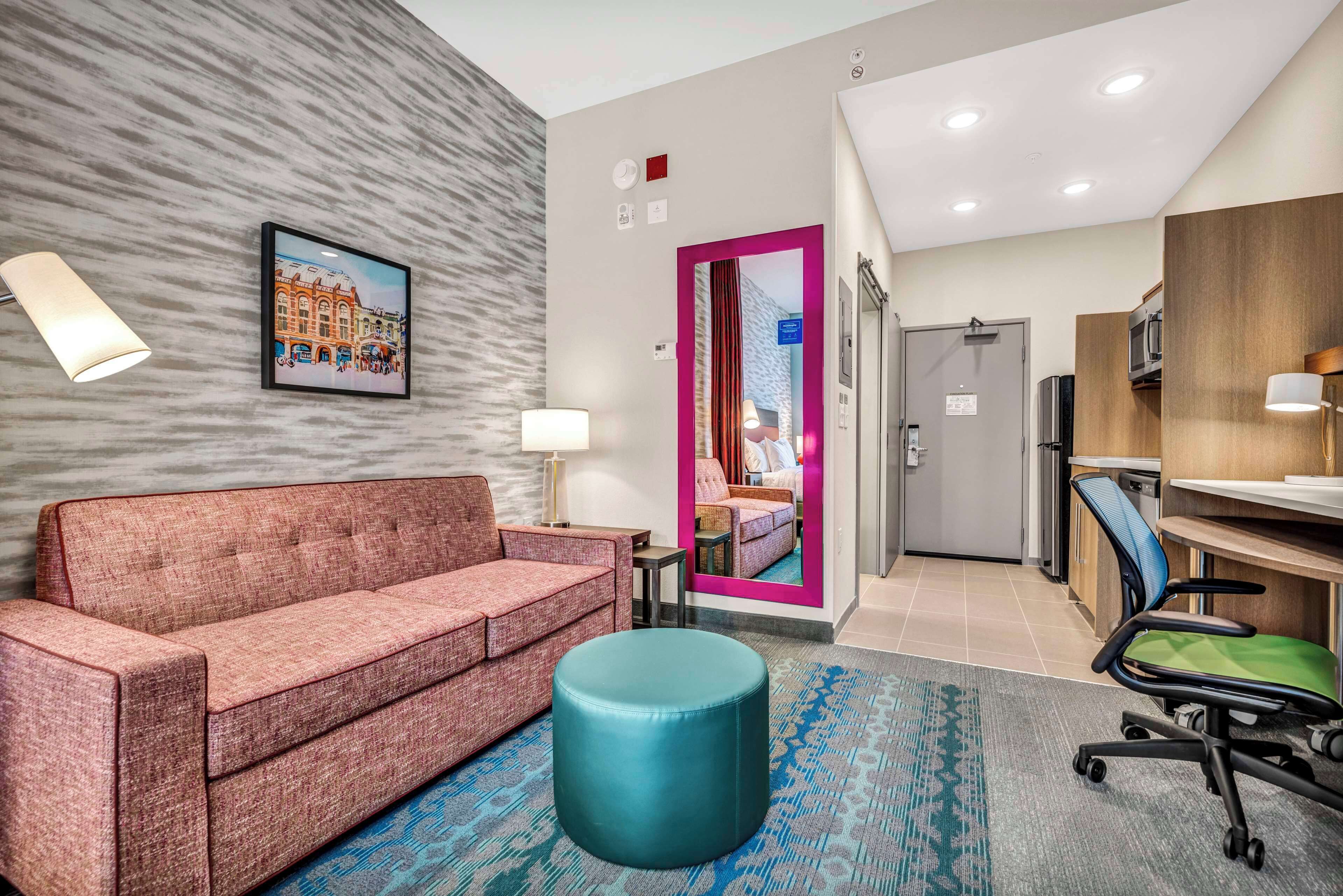 Una habitación de hotel moderna con sofá, reposapiés y un escritorio con silla.