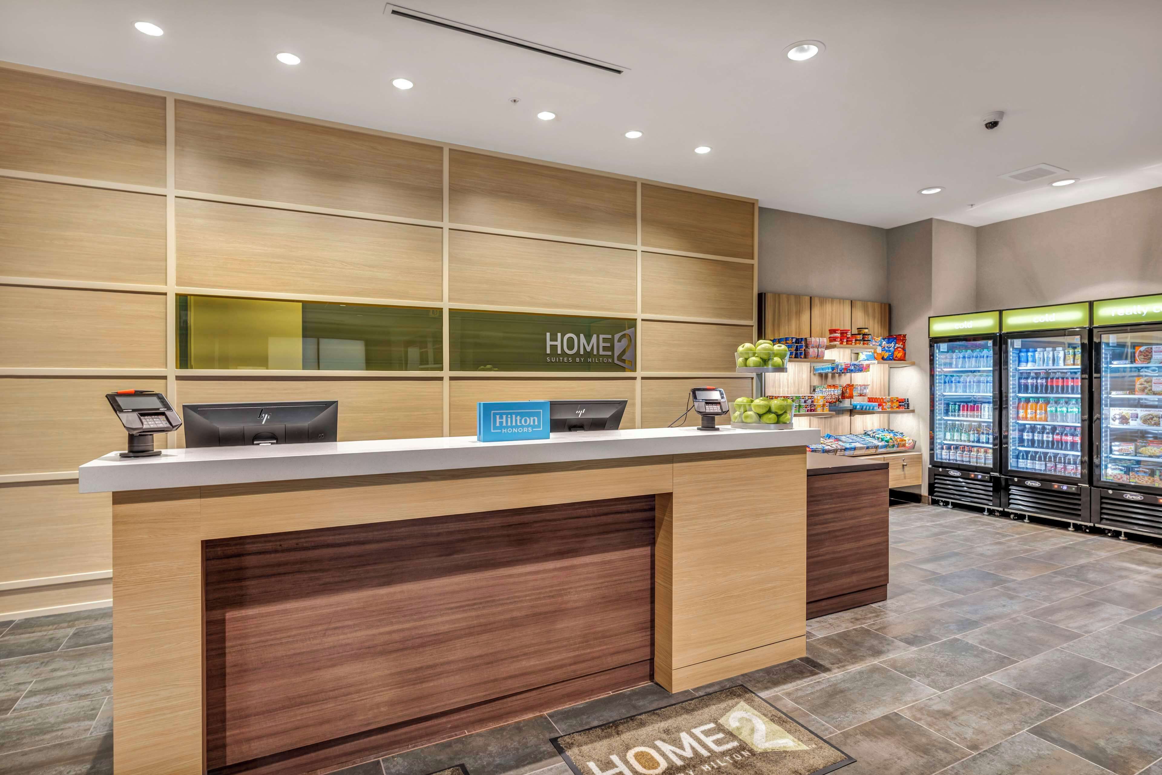 A hotel reception area with a wooden reception desk, a digital kiosk, and a minibar.