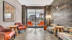 A modern lounge area with leather sofas, wooden tables, and a large window offering a view of the outdoors.
