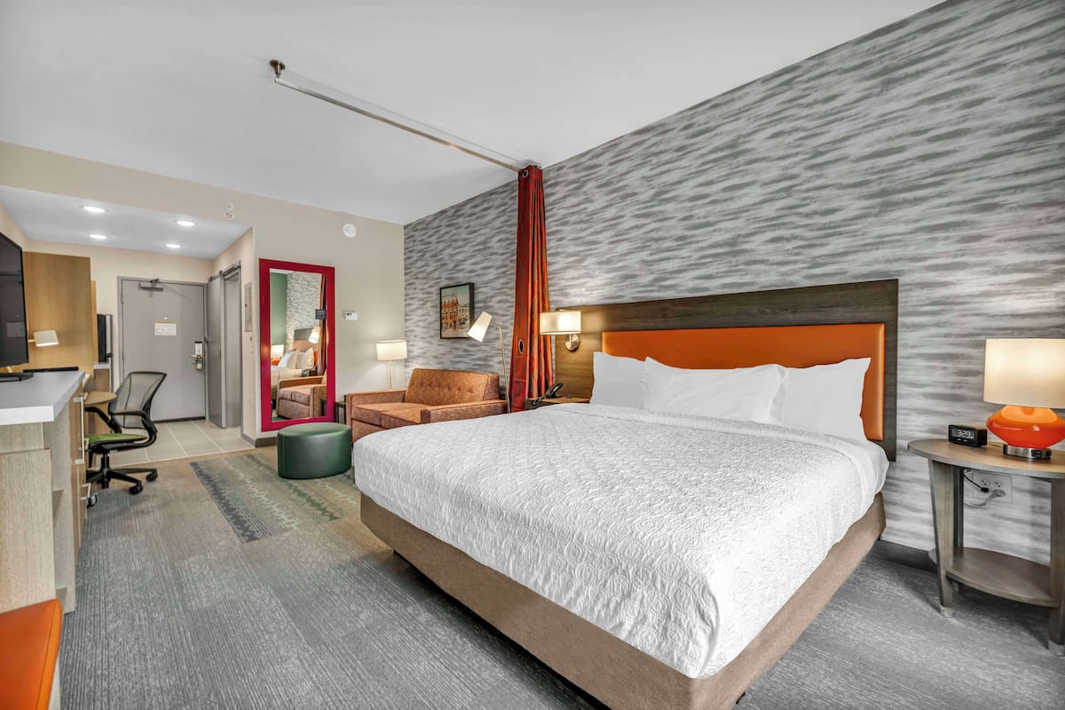 Een hotelkamer met een groot bed, een bureau, een stoel, een nachtkastje en een spiegel.