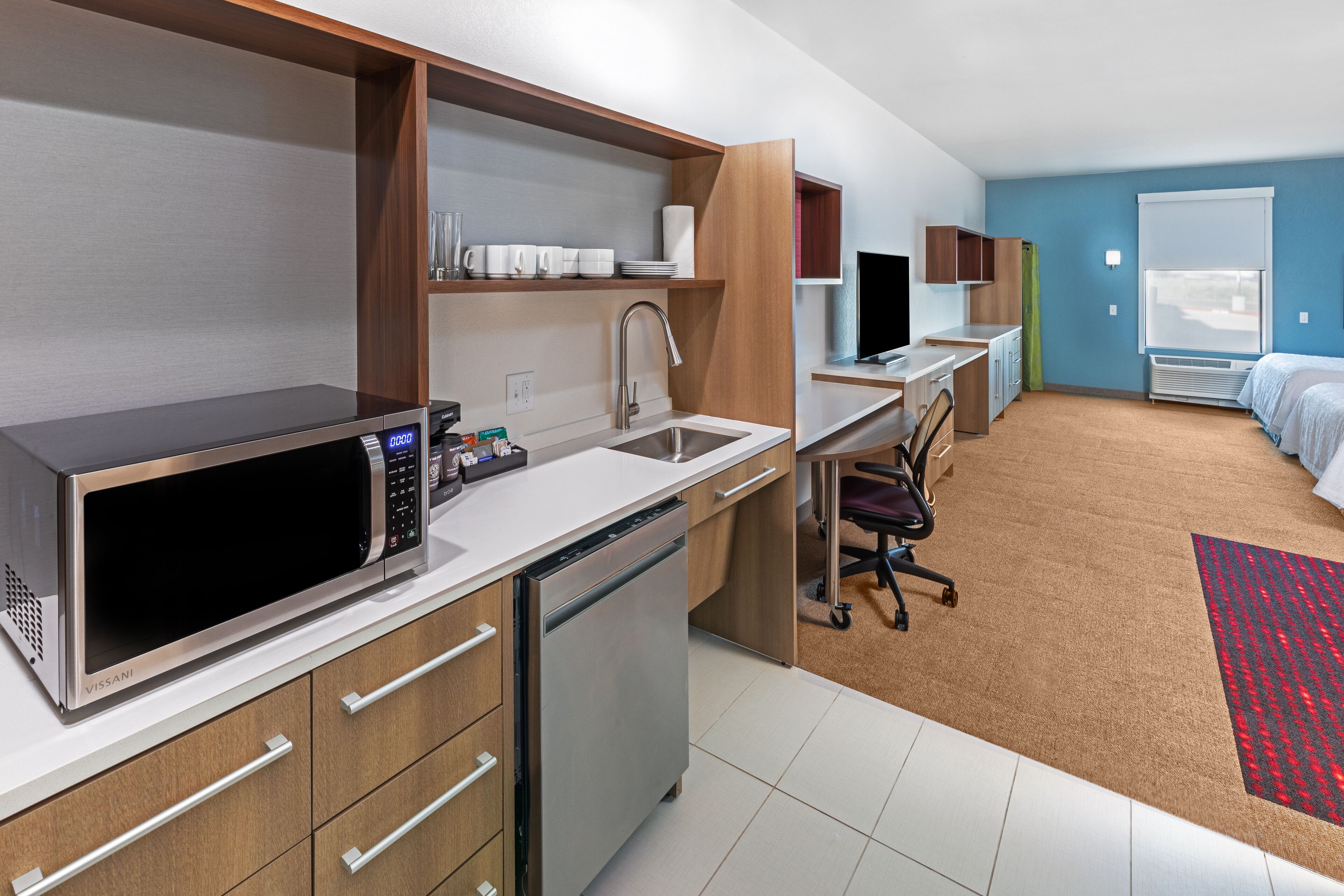 Een moderne hotelkamer met kitchenette, een bed, bureau en televisie.