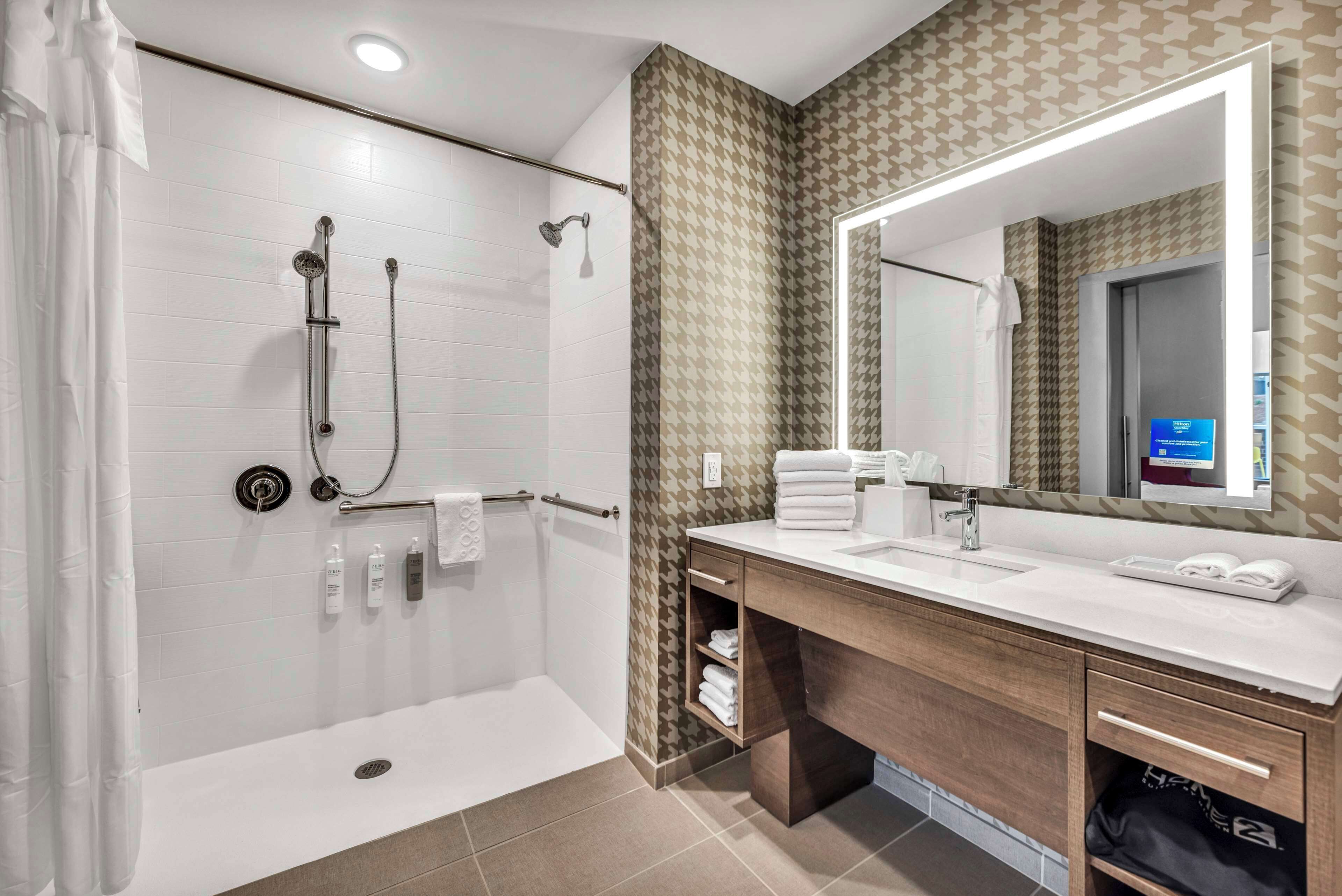 A modern bathroom with a walk-in shower, a large mirror, and a vanity with a sink and towel rack.
