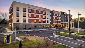 A multi-story hotel with a modern design, featuring a mix of brick and glass facades, and a parking area with a stop sign.