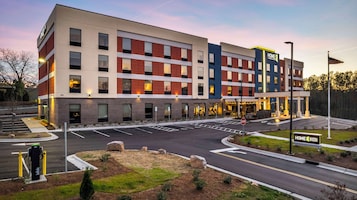 Un hotel de varios pisos con un diseño moderno, que presenta una combinación de fachadas de ladrillo y vidrio, y un área de estacionamiento con una señal de stop.