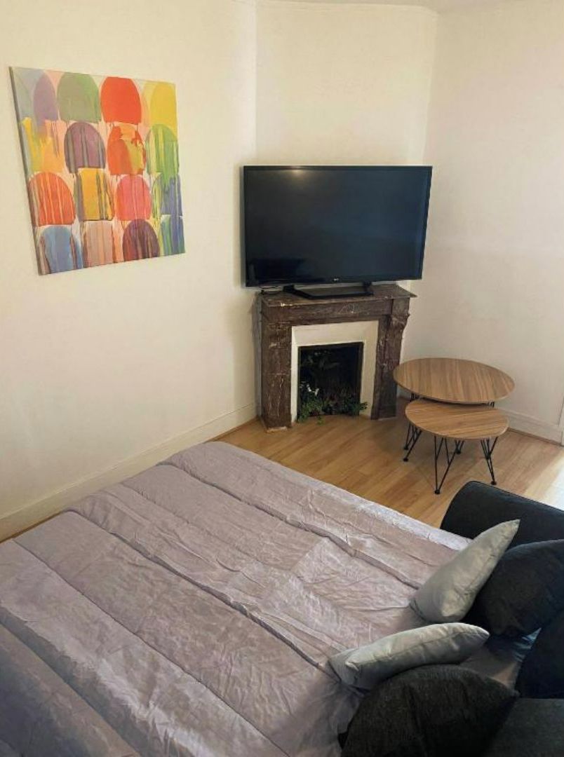Ein Zimmer mit einem Bett, einem Fernseher auf einem Kamin, einem kleinen Tisch und einem farbenfrohen Gemälde an der Wand.