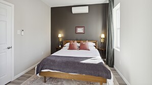Un dormitorio con cama, lámparas de noche, un cuadro enmarcado y una ventana con cortinas.