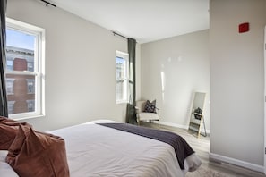Une chambre à coucher avec un lit, une chaise, un grand miroir et une fenêtre.