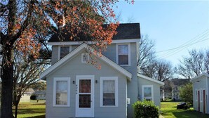A two-story house with a front porch, a small attached garage, and a well-maintained lawn. - Miss Niccies - 2BR home close to town, Lg Screened porch. NO LINENS PROVIDED (Chincoteague)