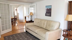 A living room with a beige sofa, a patterned rug, a wooden floor, and a poster on the wall. - Miss Niccies - 2BR home close to town, Lg Screened porch. NO LINENS PROVIDED (Chincoteague)