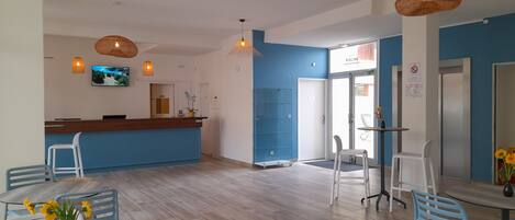 A hotel lobby with a reception desk, blue walls, wooden flooring, and modern pendant lighting.
