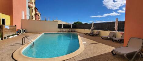 Piscina com espreguiçadeiras e área de estar coberta.