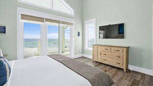 A bedroom with a large bed, a wooden dresser, a TV, and a view of the ocean through a sliding glass door. - Beach House - Sweet n Salty by PHG (Panama City Beach)