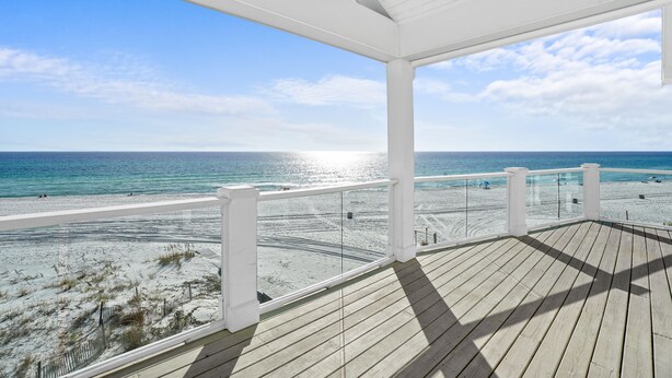 A wooden deck with a glass balustrade overlooking a beach with clear skies and calm waters. - Beach House - Sweet n Salty by PHG (Panama City Beach)