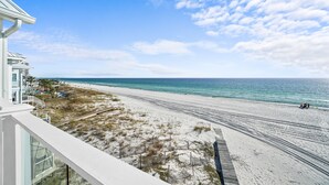 A beach view from a balcony with a clear sky, a sandy beach, and a building with a white facade. - Beach House - Sweet n Salty by PHG (Panama City Beach)