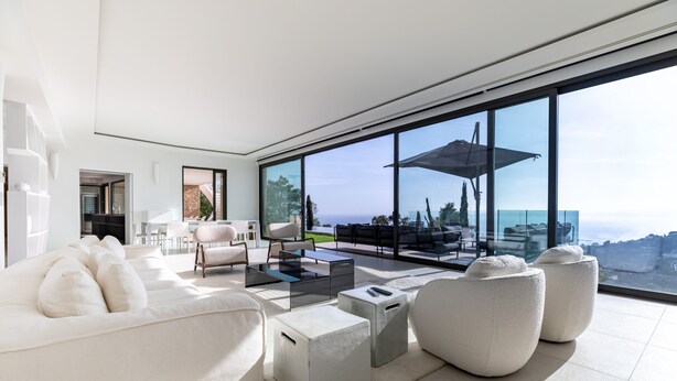 Un salón moderno con un ventanal grande, muebles blancos y vista al océano.