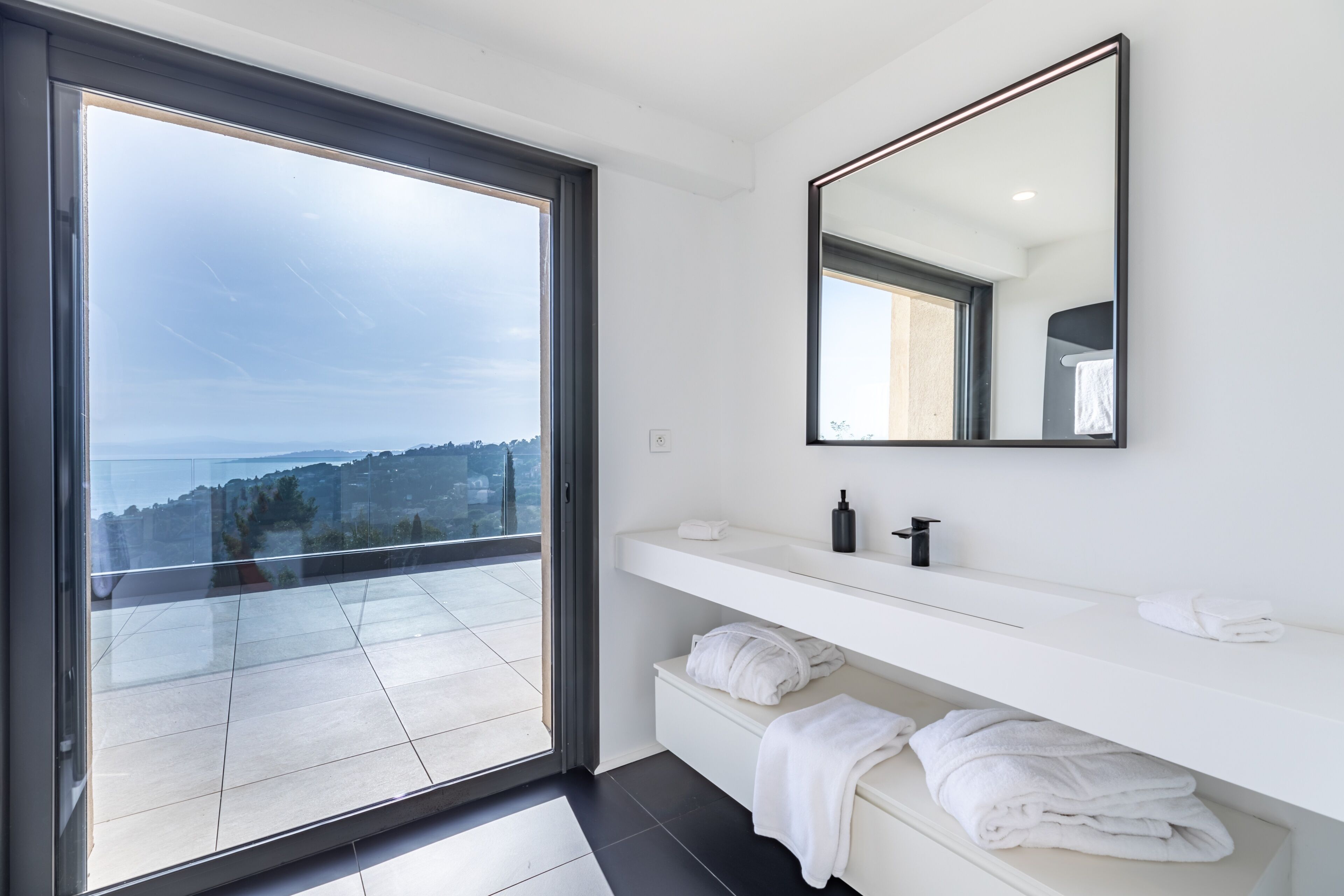 A modern bathroom with a large window, a mirror, and a white vanity with towels.
