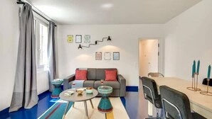 A modern living room with a grey sofa, a round coffee table, and a dining table with chairs. - Modern & colourful 3BD for 9 guests in Le Marais! (Paris)
