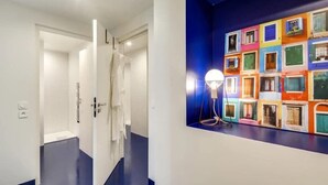 A hallway with a white door leading to a bathroom, a blue floor, and a colorful wall mural. - Modern & colourful 3BD for 9 guests in Le Marais! (Paris)