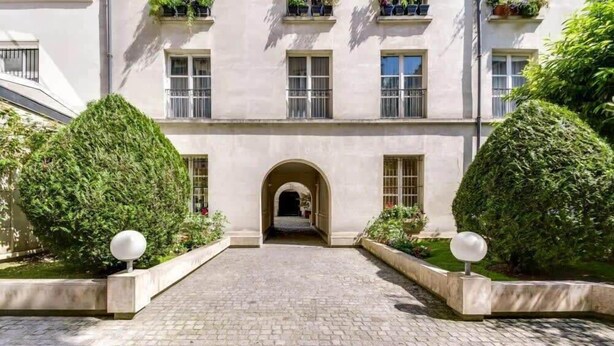 A building with a paved entrance, an arched doorway, and symmetrical landscaping with trimmed bushes and spherical bollards. - Modern & colourful 3BD for 9 guests in Le Marais! (Paris)