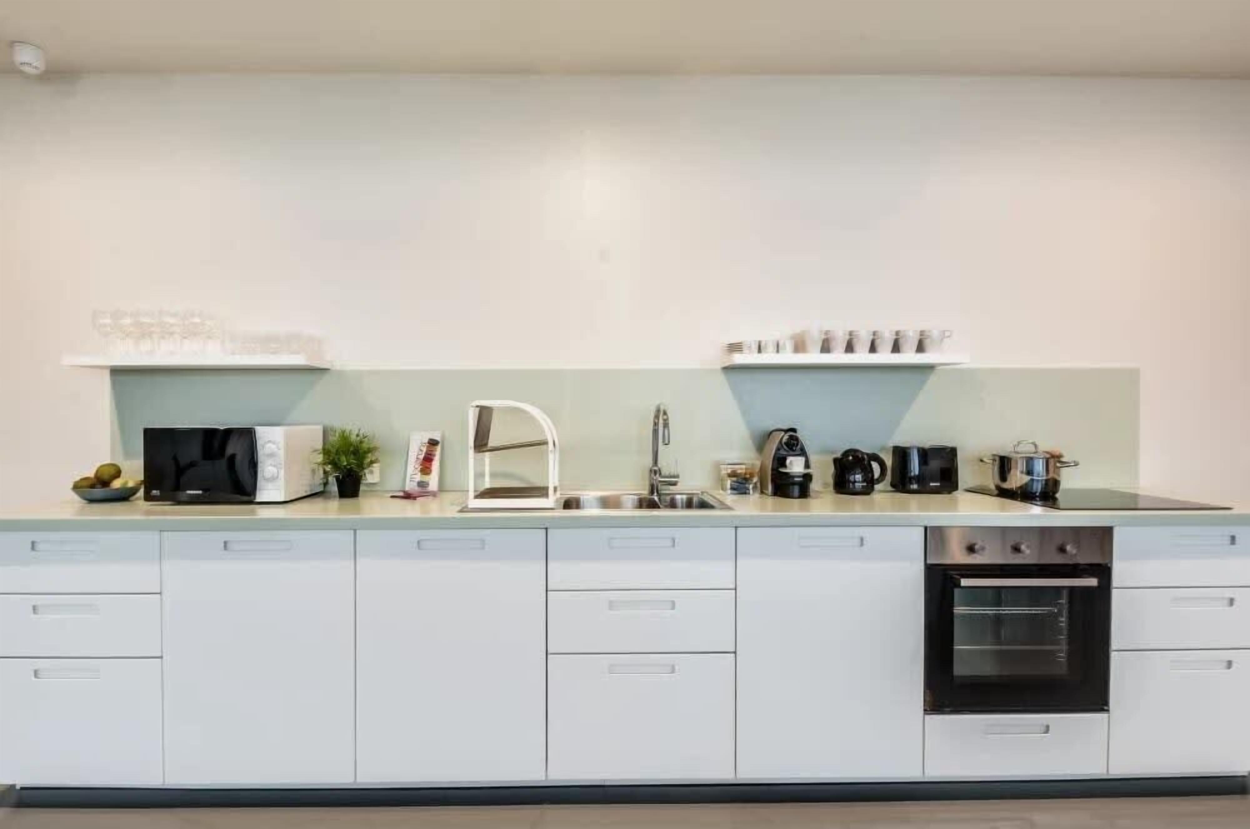 A modern kitchen with white cabinets, a built-in oven, a sink, and a coffee maker.