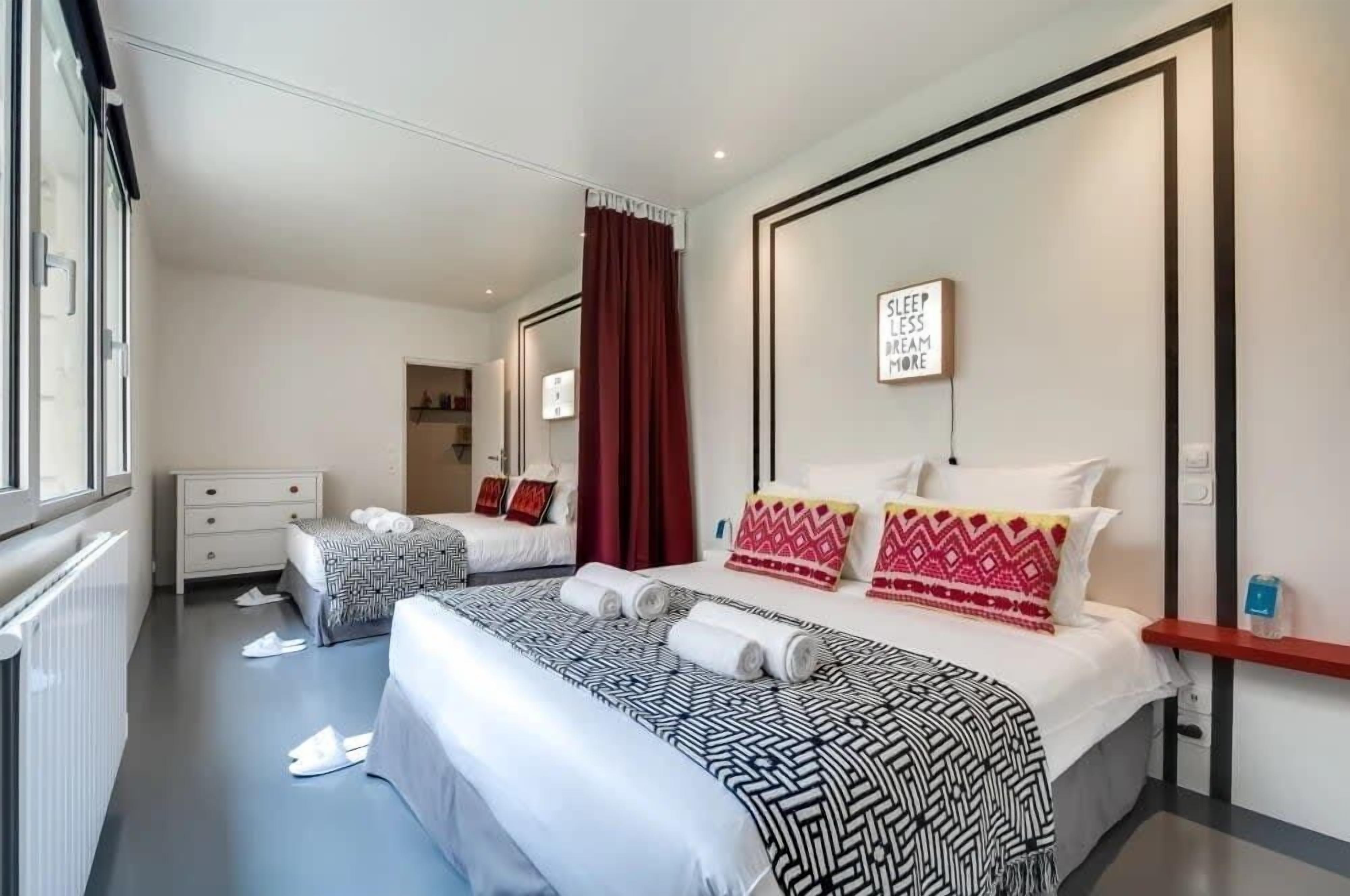 A hotel room with two beds, a large mirror, a red curtain, and a motivational quote on the wall.