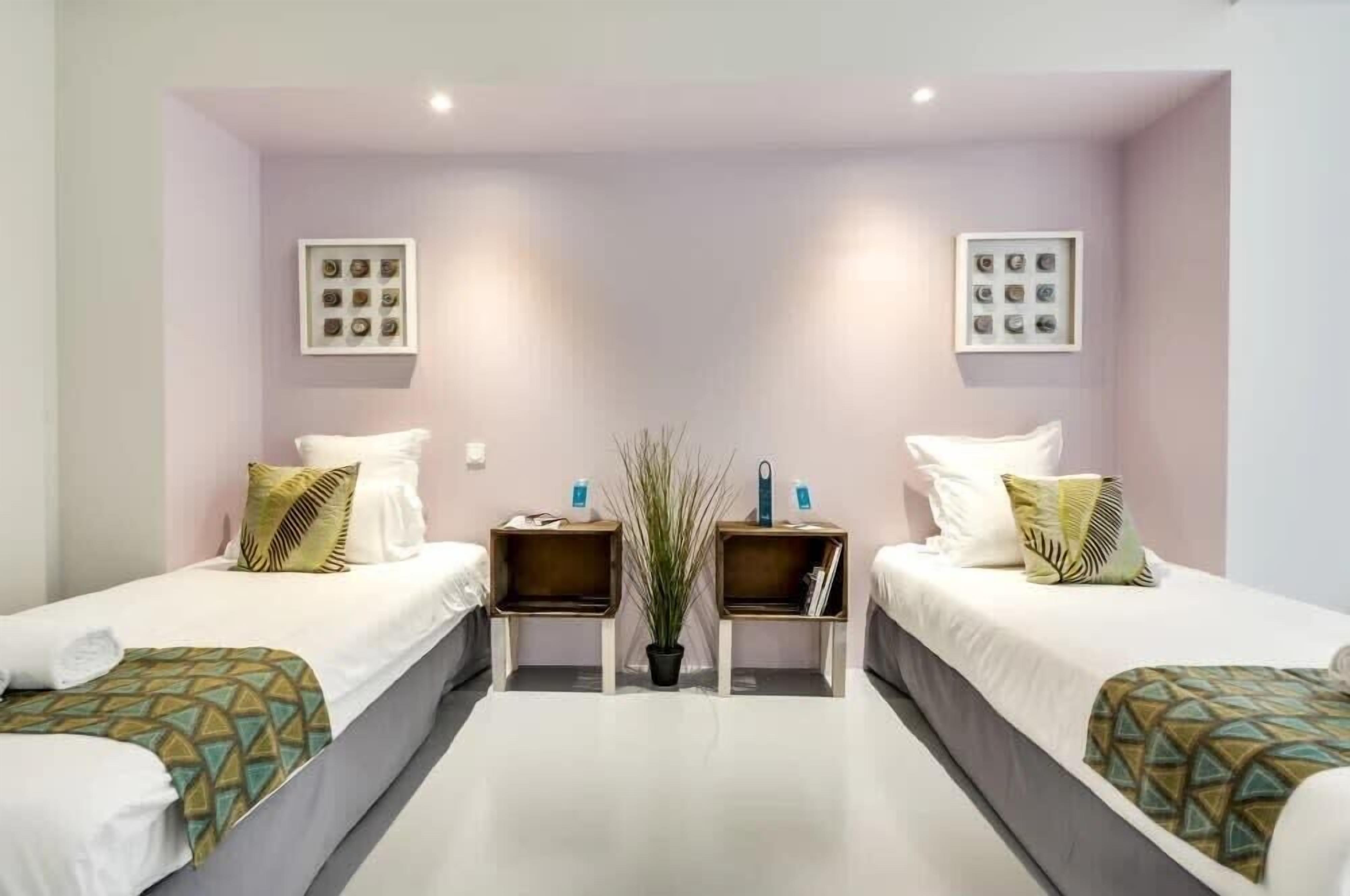 A hotel room with two single beds, a central potted plant, and two bedside tables with lamps.