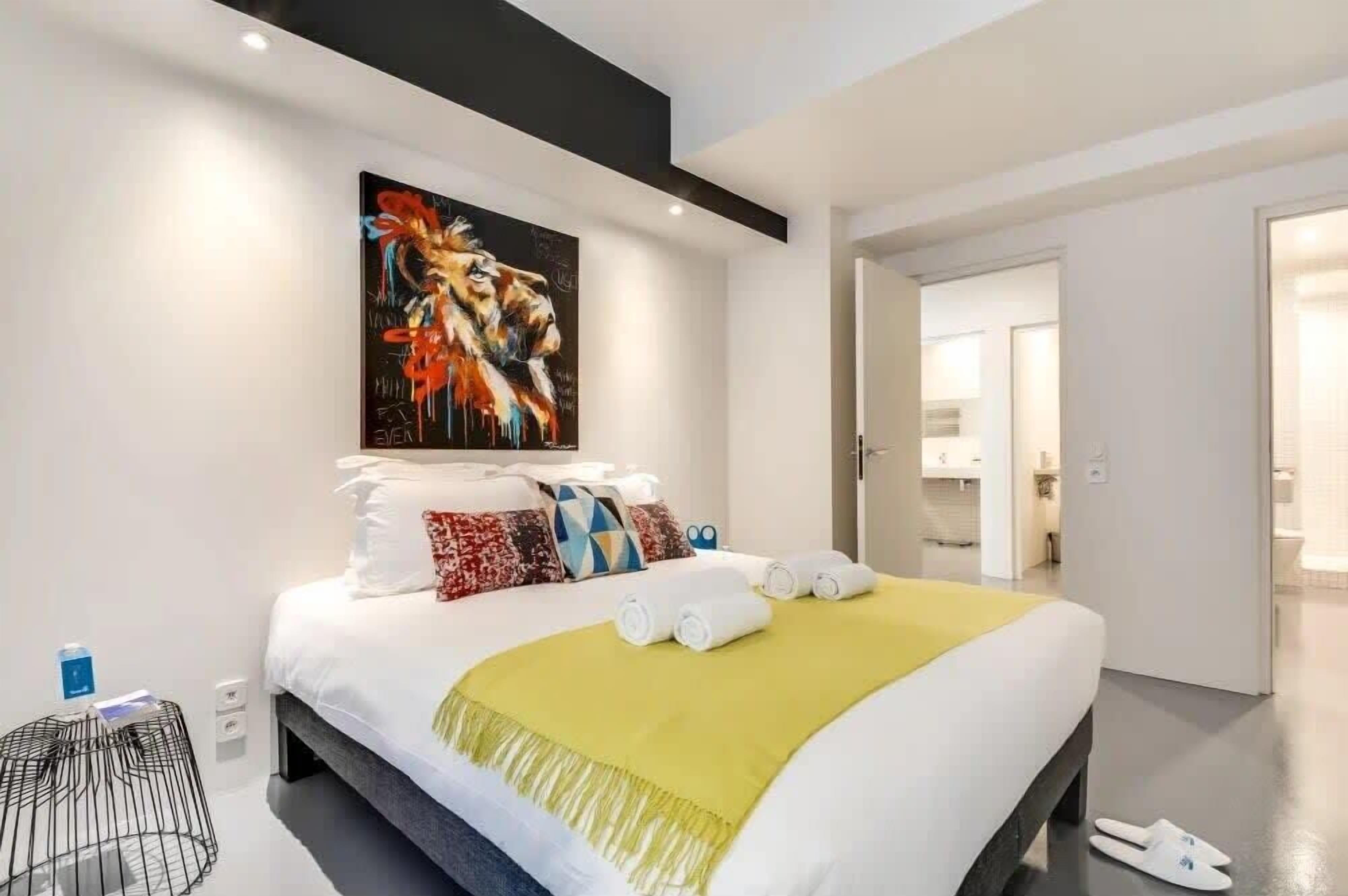 A modern hotel room with a large bed, a painting above it, and a view into the bathroom.