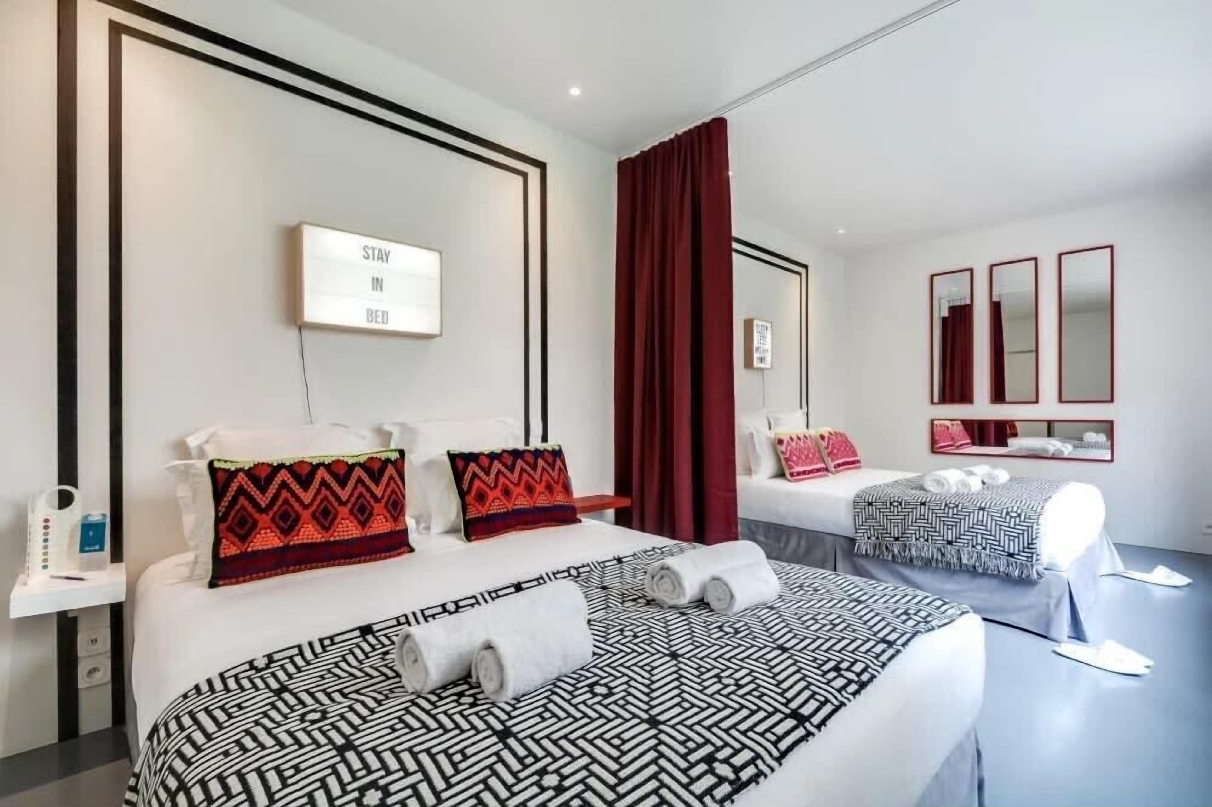 Habitación de hotel con dos camas, un espejo, un cartel en la pared y una cortina roja.
