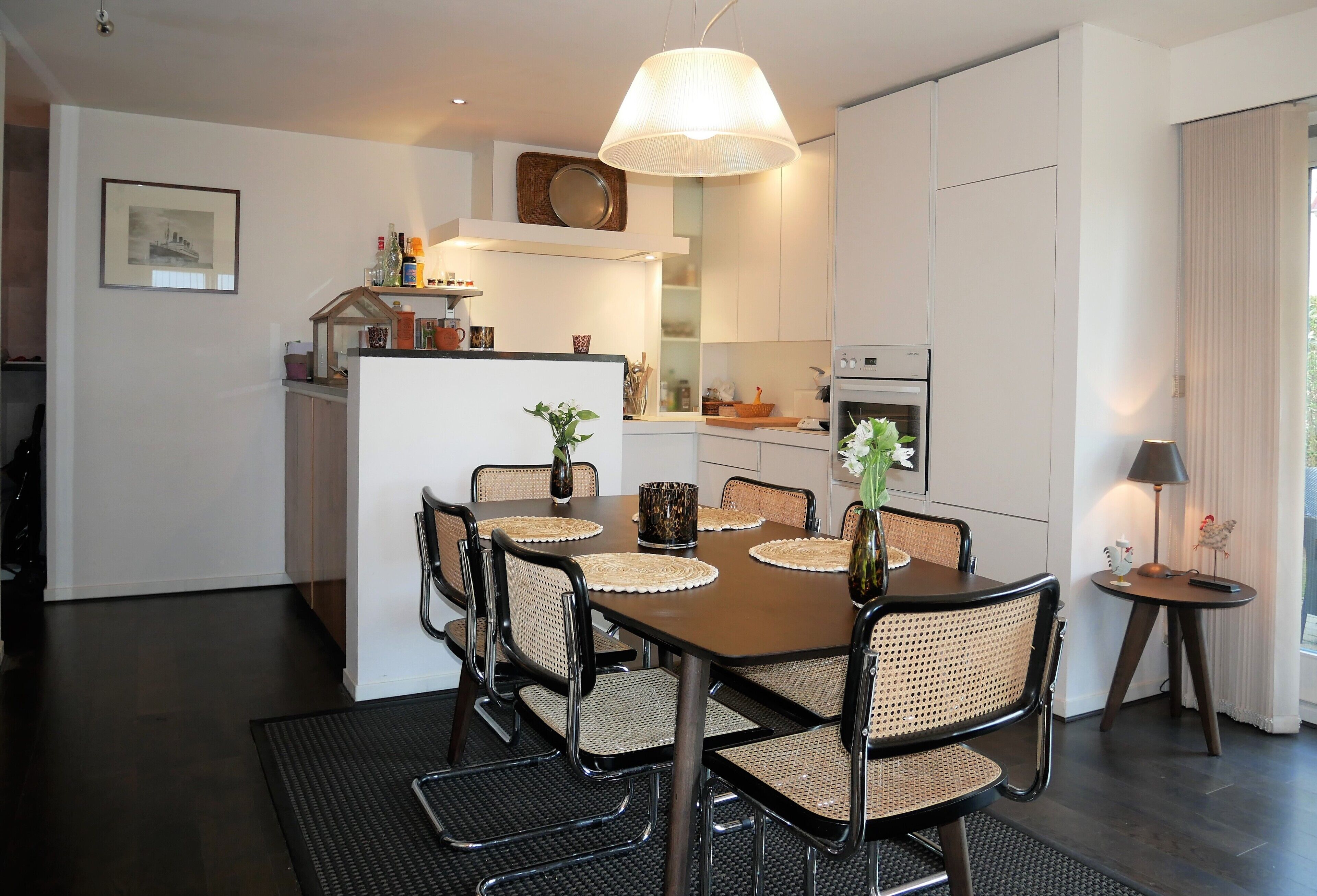 Una cocina moderna con armarios blancos, una mesa de comedor con sillas e iluminación colgante.