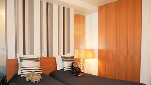 A hotel room with two beds, striped curtains, a wooden wardrobe, and a lamp. - Isabelle A1 - Bright family apartment with sunny terrace - in the concession (De Haan)