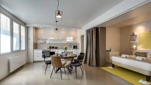 Et moderne hotelværelse med spiseplads, tekøkken og en seng med et sengebord.