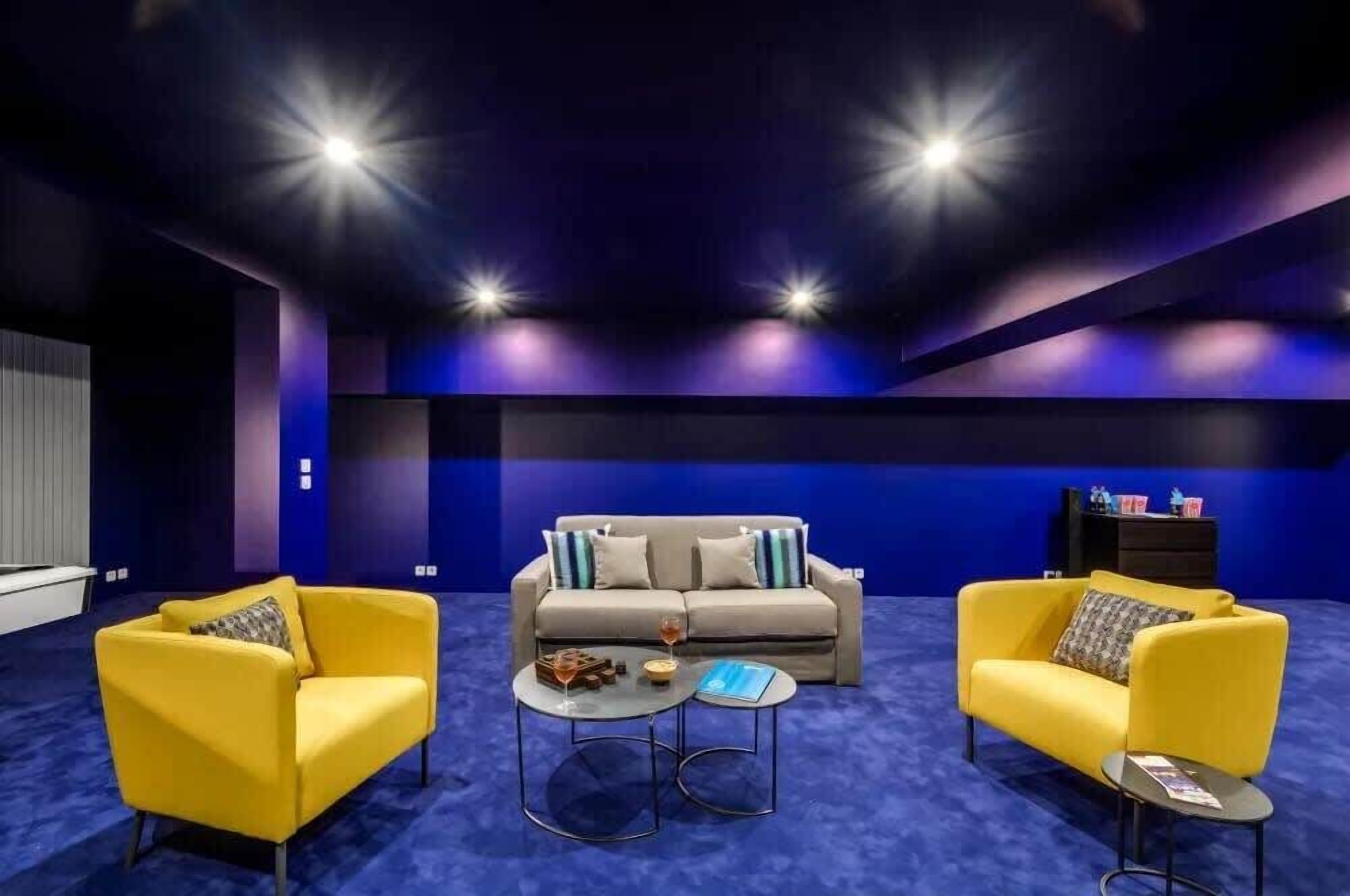 Ein modernes Wohnzimmer mit blauem Teppich, zwei gelben Armstühlen, einem grauen Sofa mit gemusterten Kissen und einem Couchtisch.