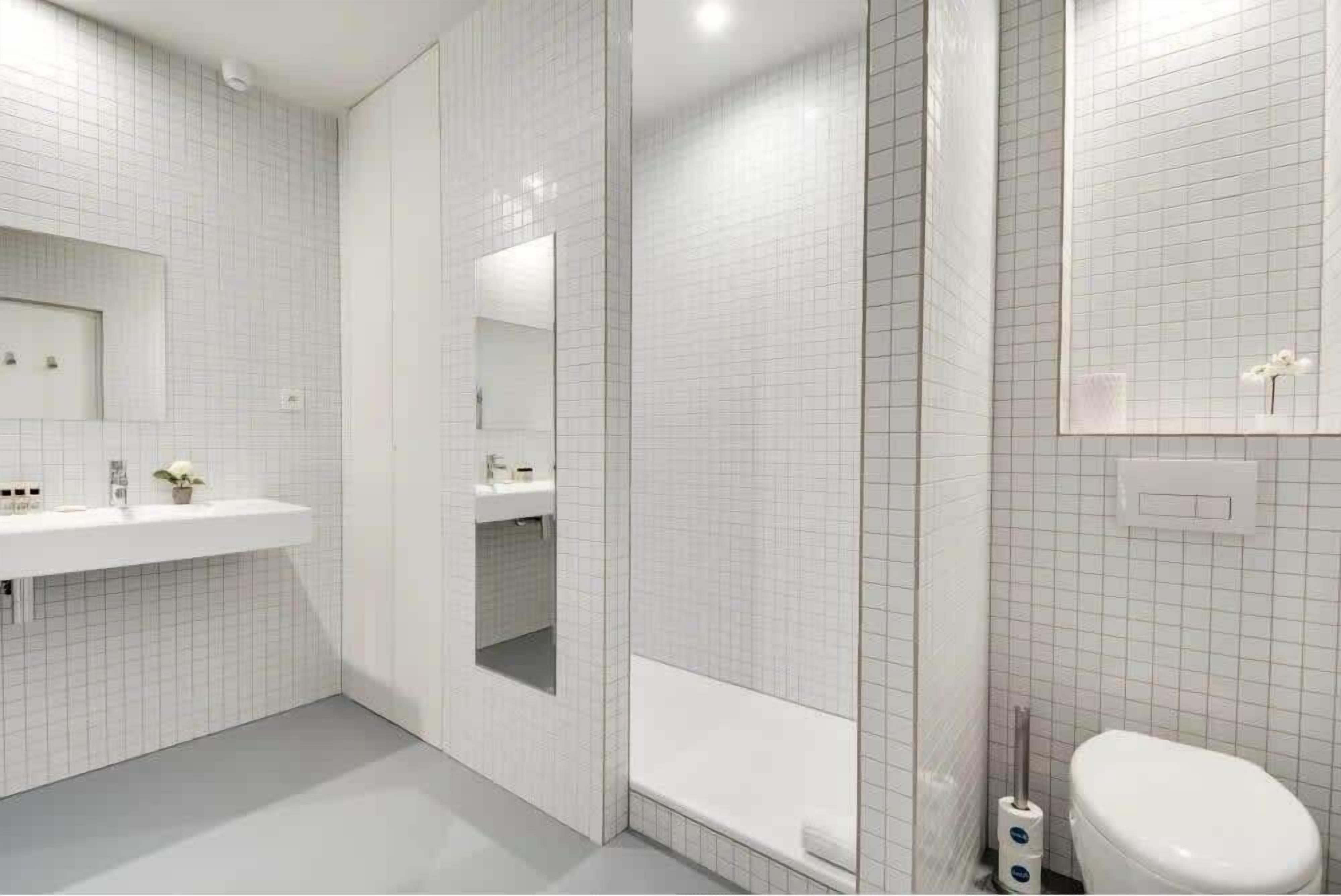 A modern bathroom with white tiled walls, a large mirror, a bathtub, and a toilet.