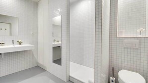 Ein modernes Badezimmer mit weißen Fliesen, einem großen Spiegel, einer Badewanne und einem WC.