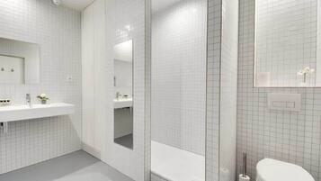 A modern bathroom with white tiled walls, a large mirror, a bathtub, and a toilet.