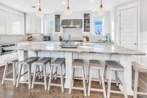 A modern kitchen with white cabinetry, a large island with bar stools, stainless steel appliances, and pendant lighting. - Seacrest "Ocean View Oasis" | 10 BR | Sleeps 28 +|Private Pool | Hot Tub | (Inlet Beach)