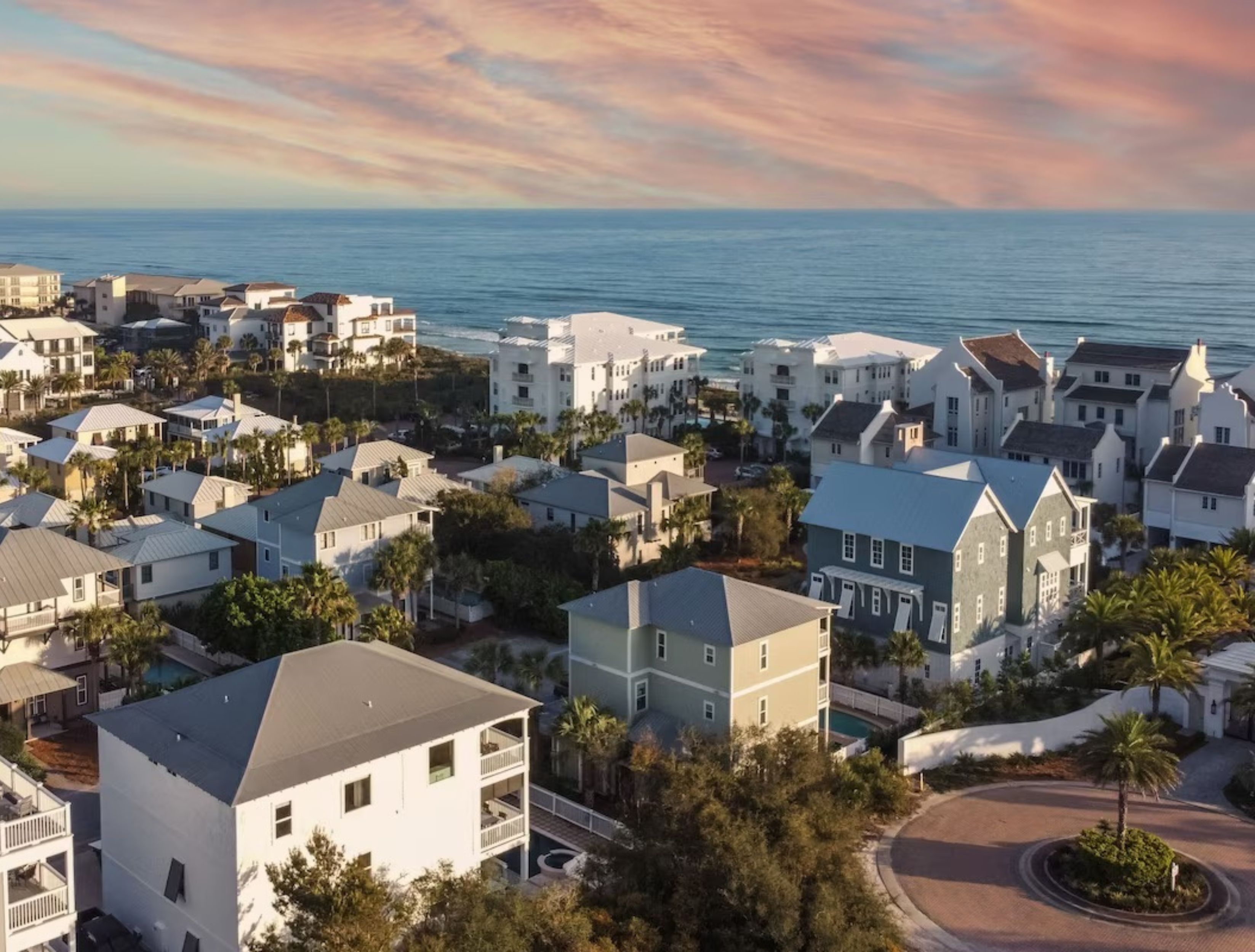 A coastal residential area with multiple two-story houses, a visible swimming pool, and a view of the ocean.