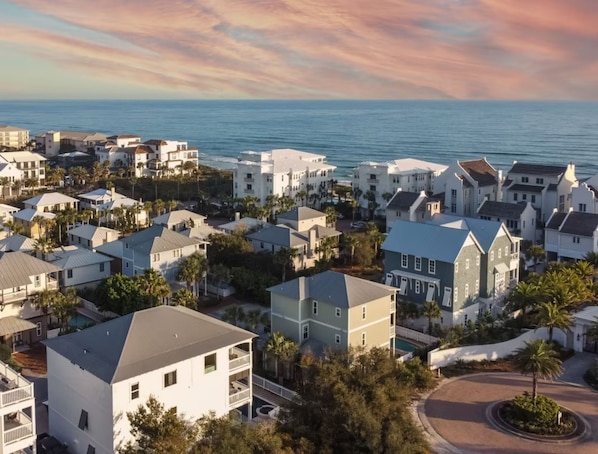Una zona residencial costera con varias casas de dos pisos, una piscina visible y vista al océano.